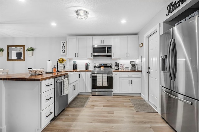 kitchen featuring wooden counters, white cabinets, light hardwood / wood-style flooring, tasteful backsplash, and stainless steel appliances