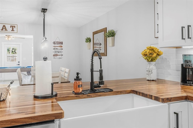 kitchen featuring butcher block counters, white cabinetry, sink, hanging light fixtures, and backsplash