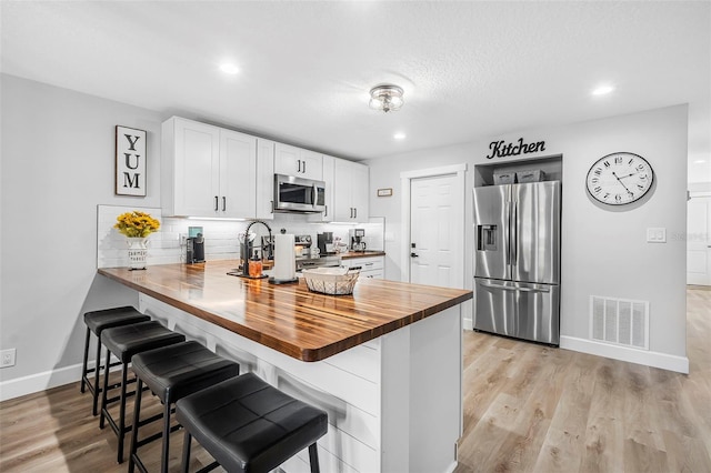 kitchen with wood counters, white cabinets, a breakfast bar area, kitchen peninsula, and stainless steel appliances