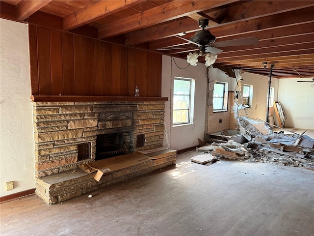 unfurnished living room with hardwood / wood-style floors, a stone fireplace, wooden ceiling, beamed ceiling, and ceiling fan