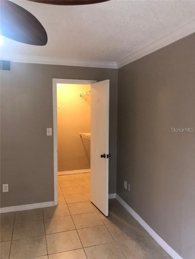 interior space with a textured ceiling, light tile patterned floors, and crown molding