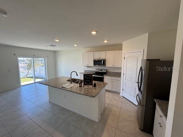 kitchen featuring stainless steel appliances, white cabinetry, dark stone countertops, and an island with sink