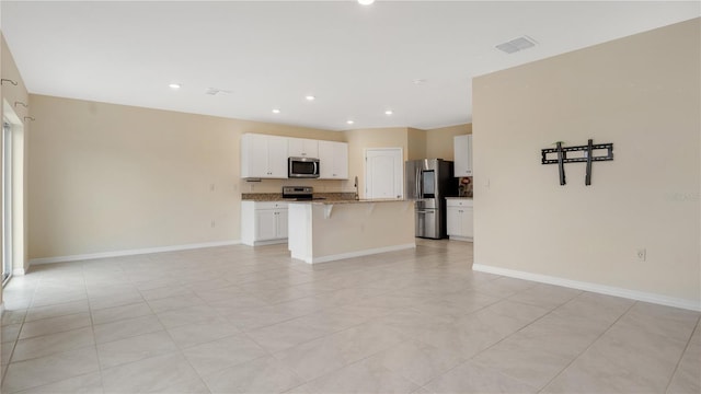 kitchen featuring appliances with stainless steel finishes, a kitchen island with sink, a kitchen breakfast bar, light stone countertops, and white cabinets