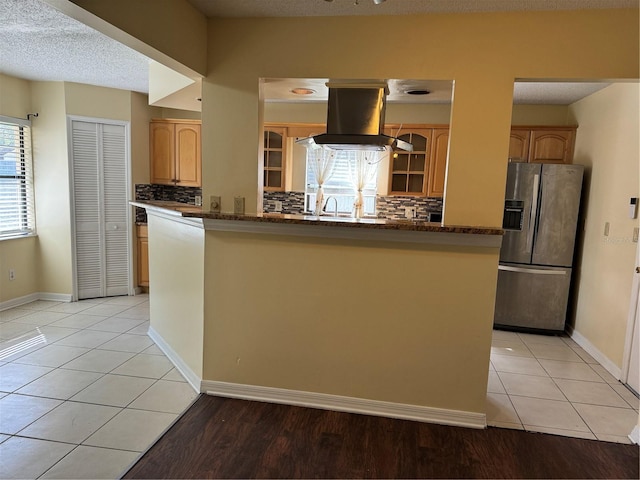 kitchen with island exhaust hood, dark stone counters, tasteful backsplash, stainless steel fridge with ice dispenser, and light tile patterned floors