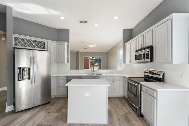 kitchen with sink, light wood-type flooring, appliances with stainless steel finishes, a kitchen island, and decorative backsplash