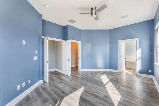 unfurnished bedroom featuring ceiling fan, connected bathroom, a spacious closet, a closet, and light wood-type flooring