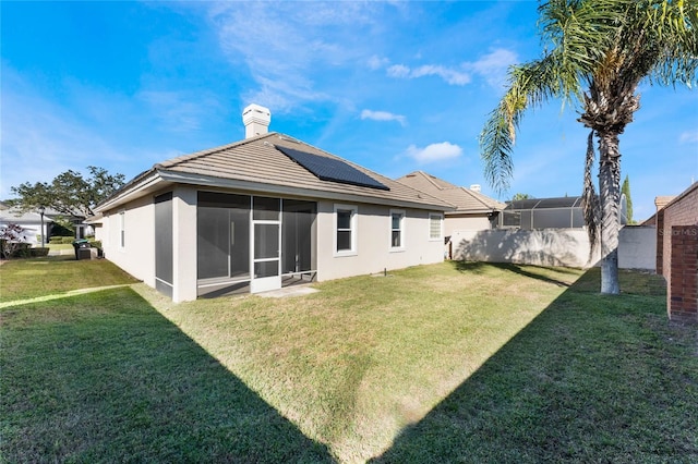 back of property featuring a sunroom, a yard, and solar panels