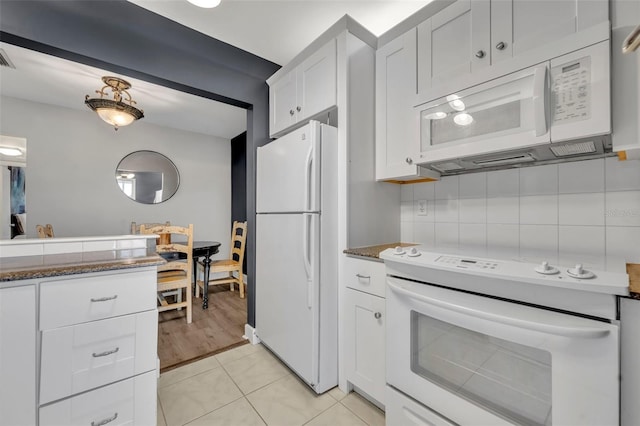 kitchen with white appliances, dark stone countertops, tasteful backsplash, light tile patterned flooring, and white cabinetry