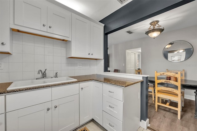 kitchen featuring dark stone countertops, white cabinetry, sink, and light hardwood / wood-style floors