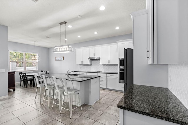 kitchen featuring hanging light fixtures, white cabinets, light tile patterned floors, and a center island with sink