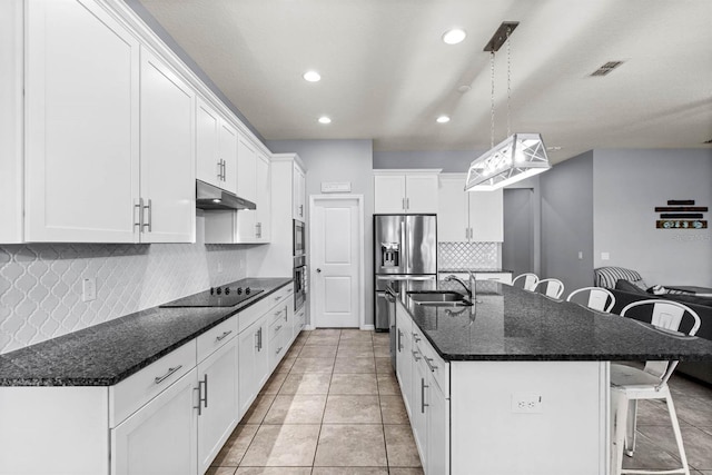 kitchen with white cabinets, decorative light fixtures, stainless steel appliances, sink, and a center island with sink