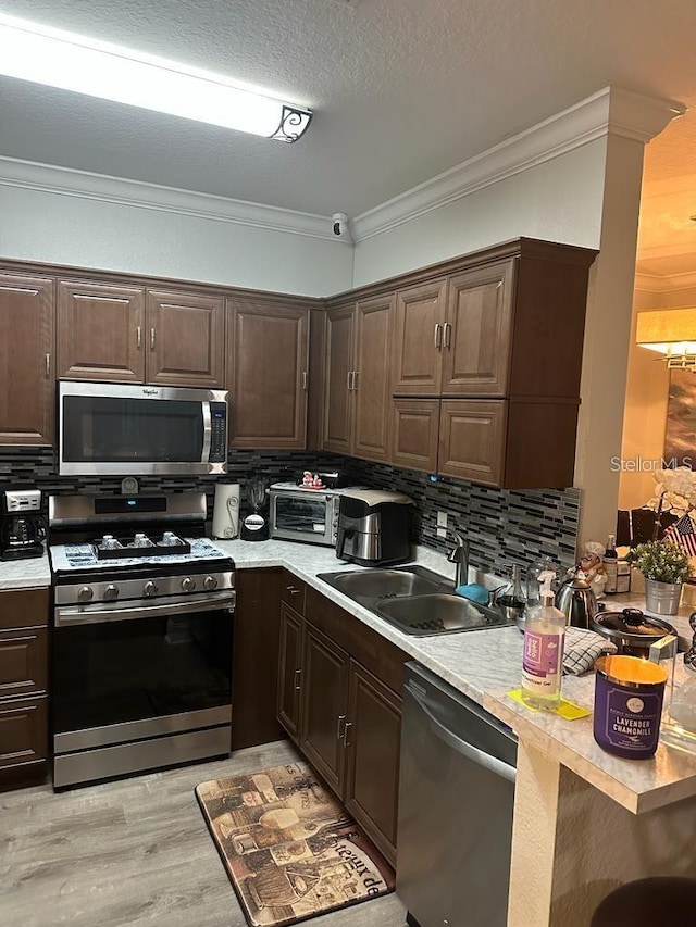 kitchen featuring dark brown cabinets, ornamental molding, sink, and appliances with stainless steel finishes