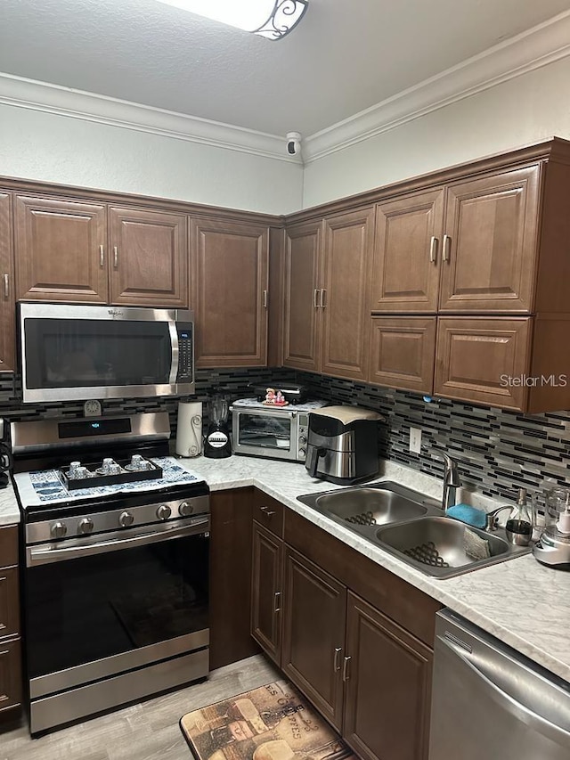 kitchen with decorative backsplash, appliances with stainless steel finishes, ornamental molding, dark brown cabinetry, and sink