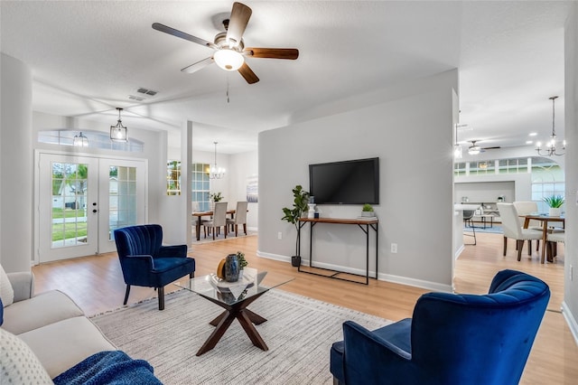 living room with french doors, ceiling fan with notable chandelier, and light hardwood / wood-style floors