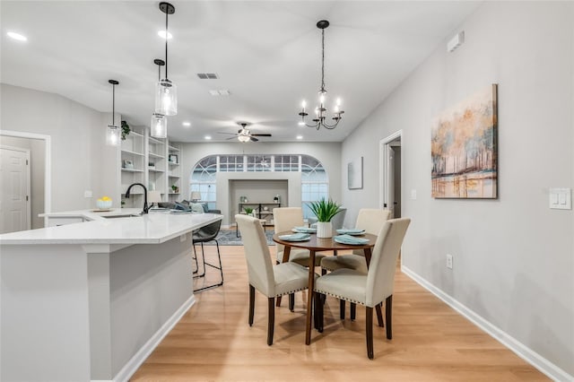 dining area with ceiling fan with notable chandelier, sink, and light wood-type flooring