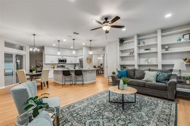 living room with ceiling fan with notable chandelier and light hardwood / wood-style flooring