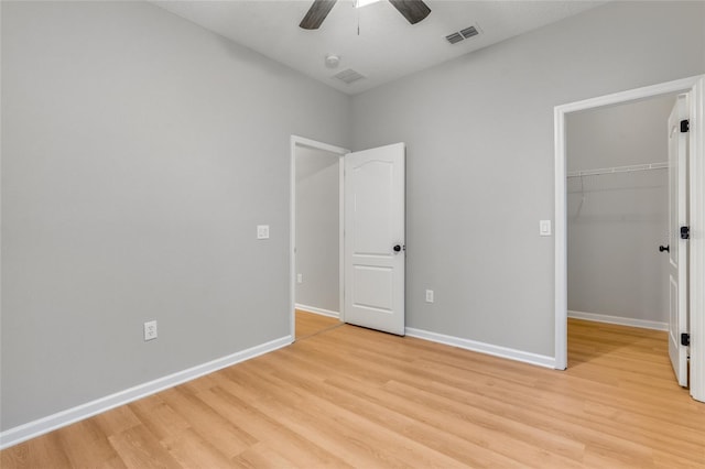 unfurnished bedroom featuring ceiling fan, a walk in closet, a closet, and light hardwood / wood-style floors