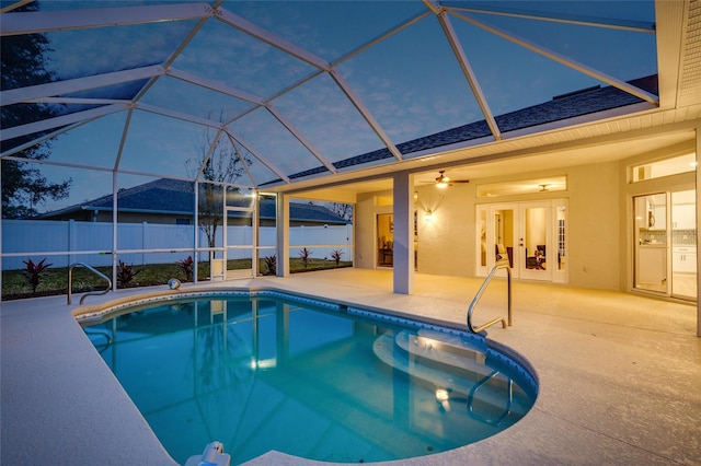 pool at dusk with glass enclosure, a patio area, and ceiling fan