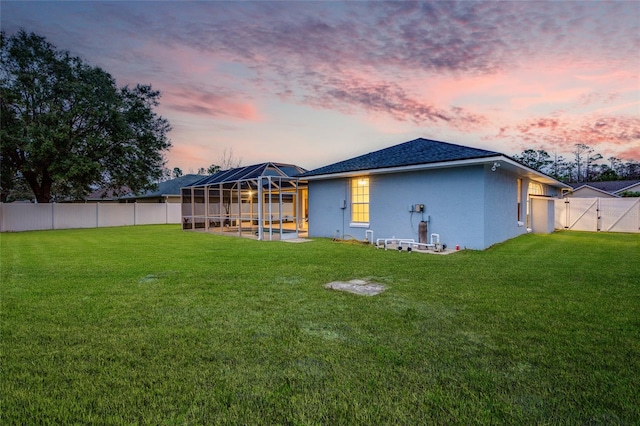 back house at dusk with a lanai, a yard, and a patio