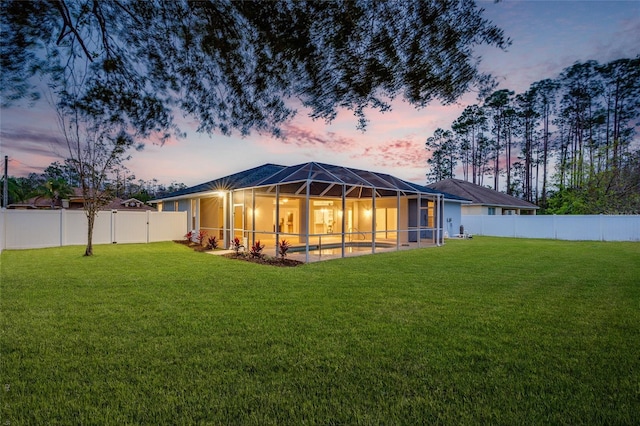 back house at dusk featuring glass enclosure and a yard