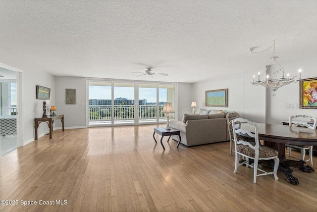 living room featuring ceiling fan with notable chandelier, a textured ceiling, light hardwood / wood-style flooring, and floor to ceiling windows