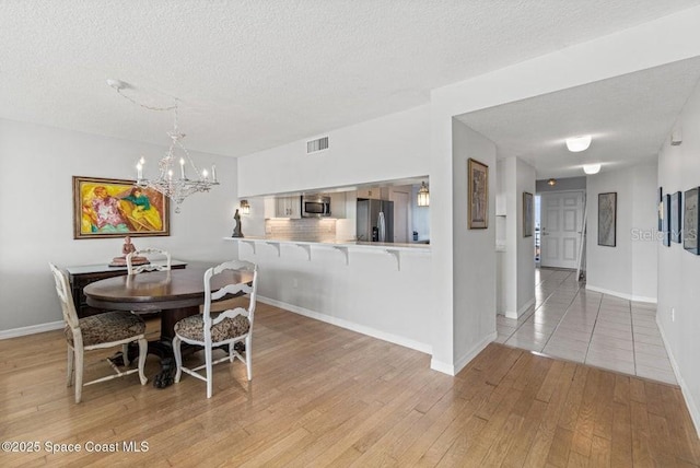 dining area with wood-type flooring, a textured ceiling, and an inviting chandelier