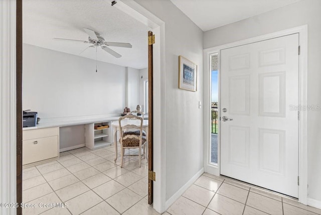 tiled foyer with ceiling fan, built in desk, and a textured ceiling