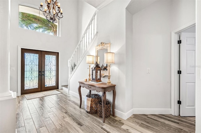 foyer featuring a towering ceiling, light hardwood / wood-style floors, french doors, and a notable chandelier