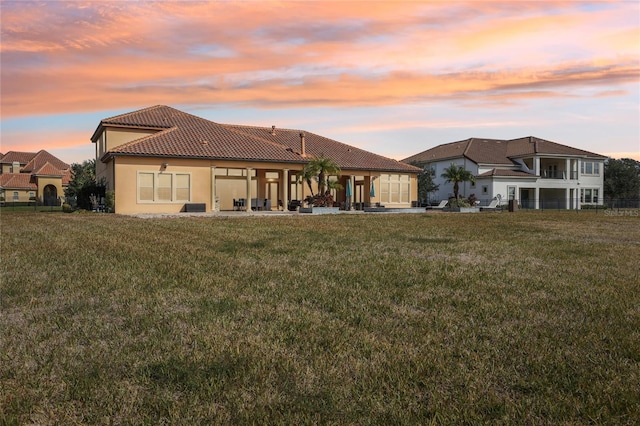 back house at dusk featuring a lawn