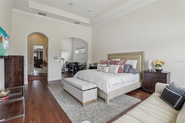 bedroom with baseboards, visible vents, arched walkways, dark wood-type flooring, and a tray ceiling