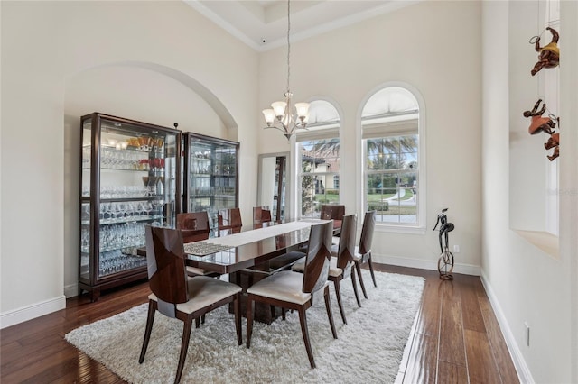 dining area featuring dark wood-style flooring, a towering ceiling, baseboards, and an inviting chandelier