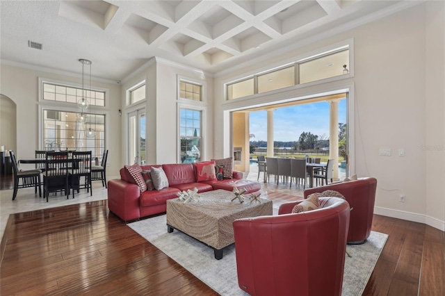 living room featuring baseboards, arched walkways, a towering ceiling, ornamental molding, and wood finished floors