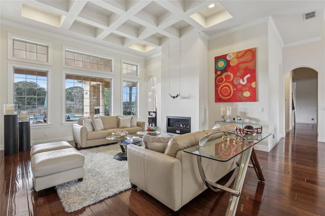 living area with arched walkways, a high ceiling, a glass covered fireplace, visible vents, and dark wood finished floors