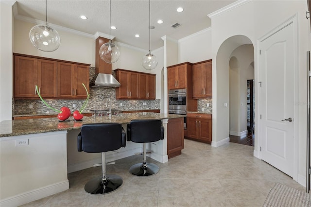 kitchen featuring stainless steel double oven, decorative light fixtures, and dark stone countertops