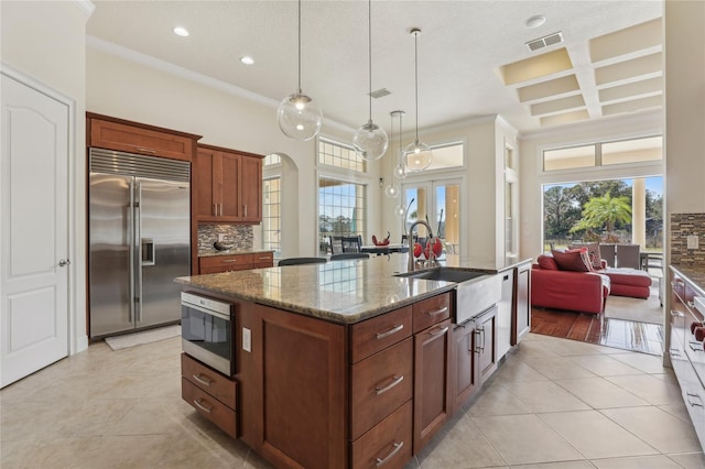 kitchen featuring a center island with sink, visible vents, coffered ceiling, built in appliances, and a sink