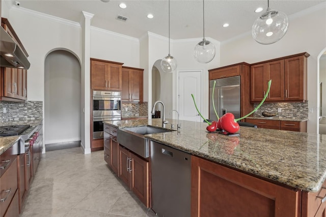 kitchen featuring arched walkways, decorative light fixtures, stainless steel appliances, a kitchen island with sink, and a sink