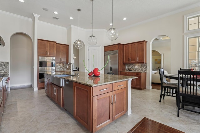 kitchen with a center island with sink, arched walkways, hanging light fixtures, stainless steel appliances, and a sink