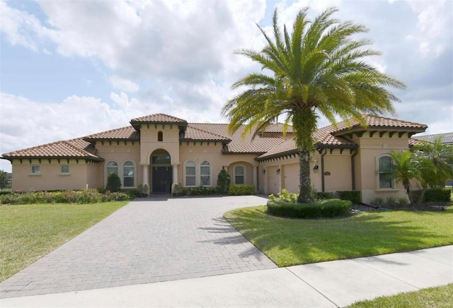 mediterranean / spanish-style home with an attached garage, a tile roof, decorative driveway, stucco siding, and a front yard