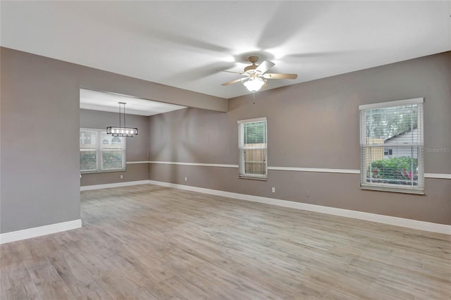 empty room with light hardwood / wood-style flooring and ceiling fan with notable chandelier