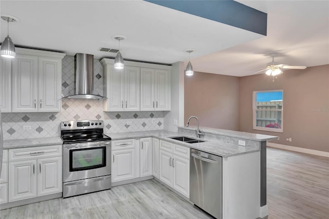 kitchen with appliances with stainless steel finishes, kitchen peninsula, pendant lighting, wall chimney exhaust hood, and sink