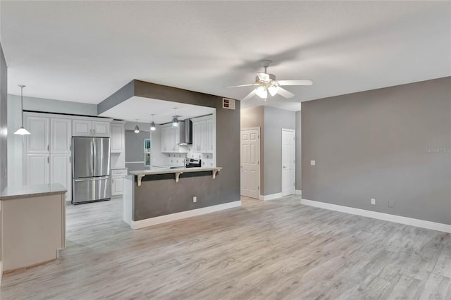 kitchen with hanging light fixtures, light wood-type flooring, a breakfast bar area, white cabinets, and appliances with stainless steel finishes