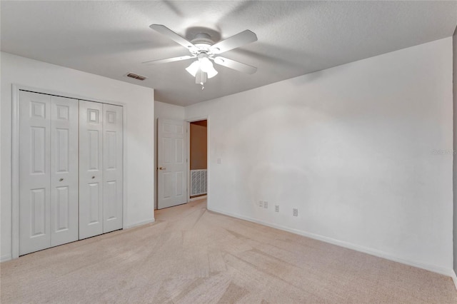 unfurnished bedroom featuring ceiling fan, a closet, light carpet, and a textured ceiling