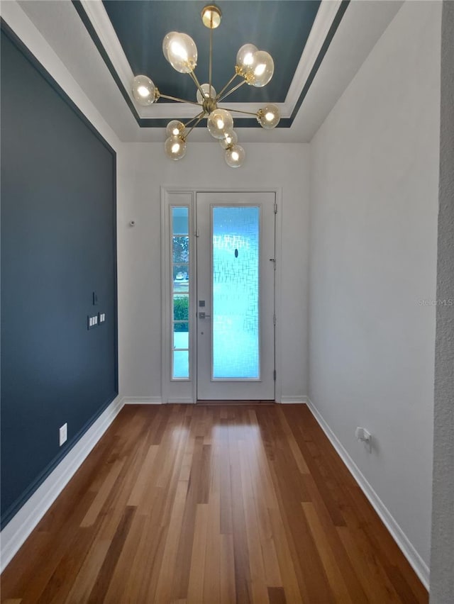 doorway with wood-type flooring, a raised ceiling, and a chandelier