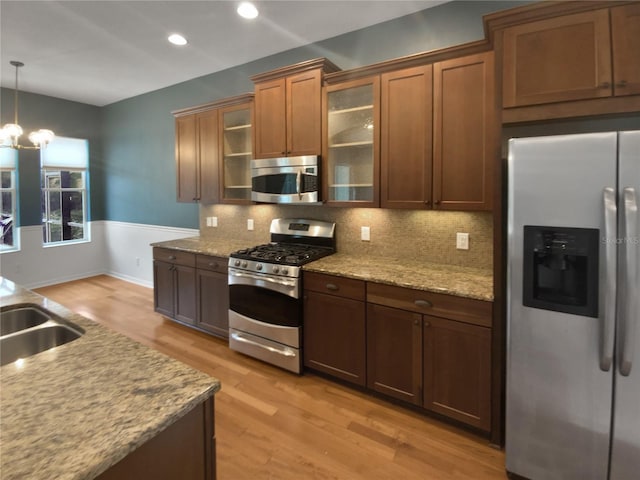 kitchen with stainless steel appliances, light wood-type flooring, light stone countertops, a notable chandelier, and pendant lighting