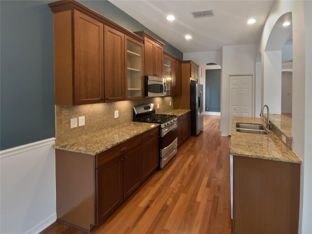 kitchen with light hardwood / wood-style floors, stainless steel appliances, light stone counters, sink, and backsplash