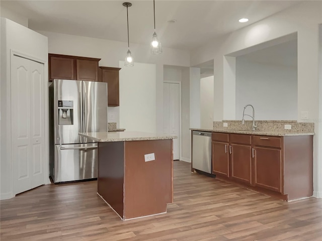 kitchen with stainless steel appliances, light stone countertops, kitchen peninsula, pendant lighting, and sink