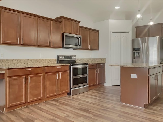 kitchen featuring light stone countertops, light hardwood / wood-style flooring, pendant lighting, a kitchen island, and appliances with stainless steel finishes