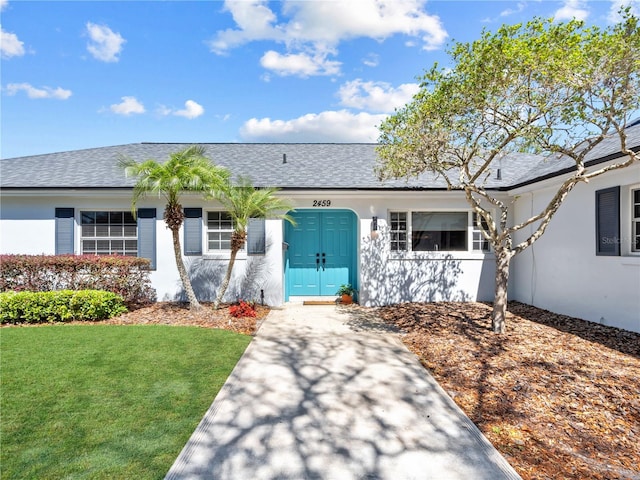 ranch-style home with a front lawn, a shingled roof, and stucco siding