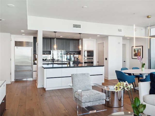 kitchen featuring white cabinetry, hanging light fixtures, a center island, built in appliances, and wood-type flooring