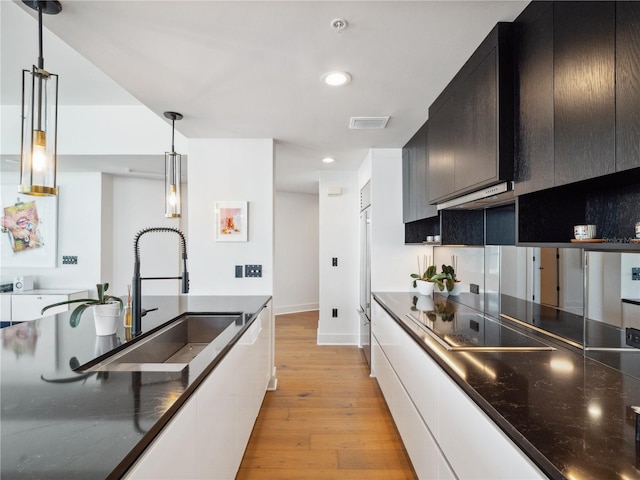 kitchen featuring sink, light hardwood / wood-style flooring, high end fridge, hanging light fixtures, and black electric cooktop